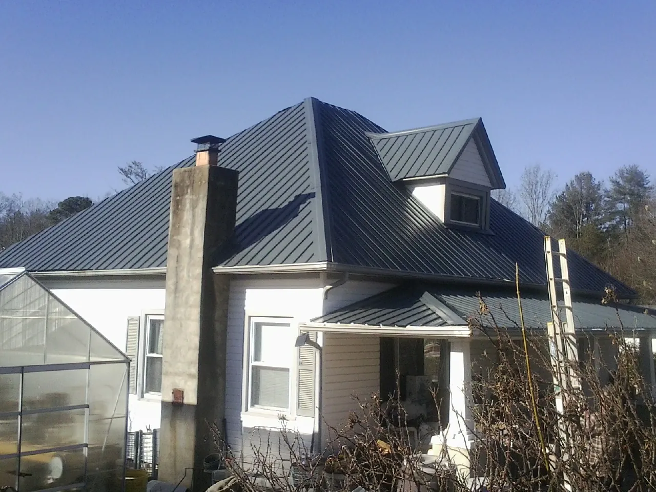 Dark blue standing seam metal roof on a white farmhouse with dormer — Slate & Tile Roof Repair by Roofing Brothers in South Royalton
