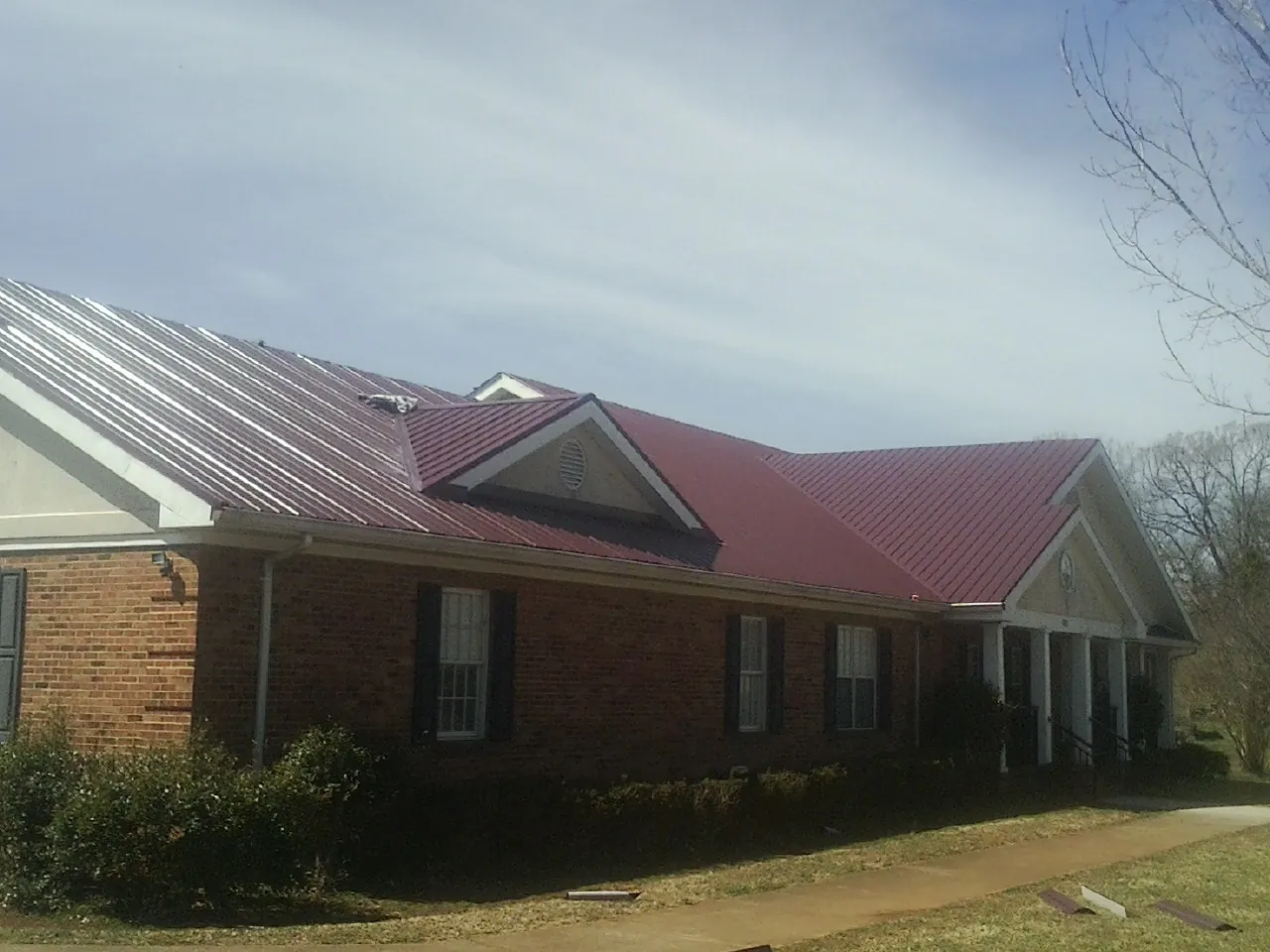 Red metal roof with gabled entries on a long brick building, from a Hail Damage Roof Repair job in South Royalton
