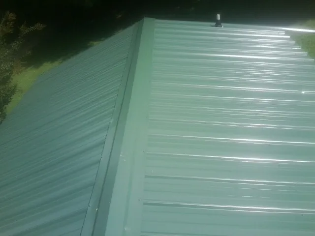 New green metal panels meeting at the ridge of a roof — Flat Roof Repair work by our crew in South Royalton