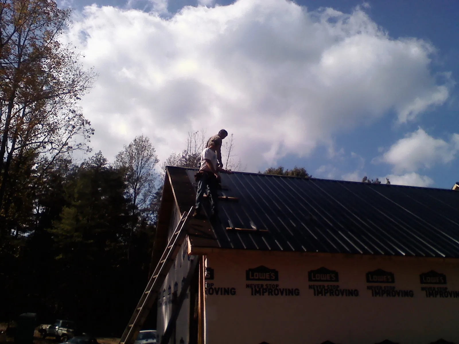 Roofer fastening dark metal panels high against a cloudy sky, from a Roof Inspection job in South Royalton