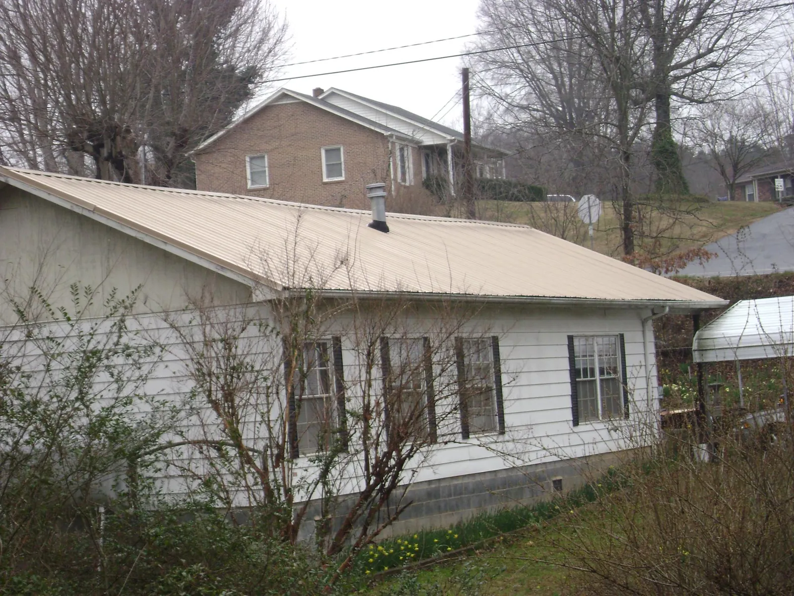 Tan metal roof on a white sided house set into a hillside — Commercial Roofing by Roofing Brothers in South Royalton